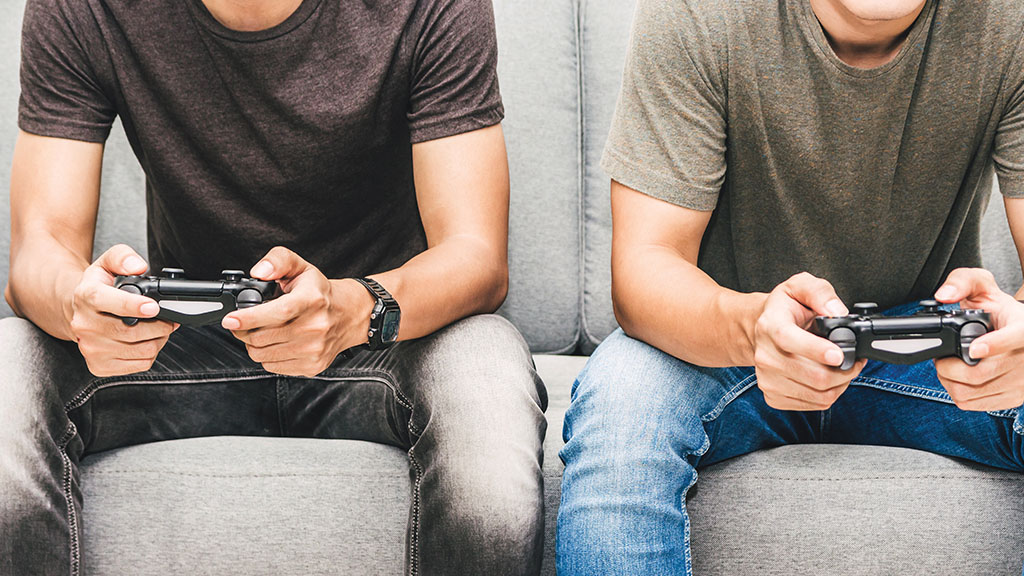 The lower half of two teenage boys holding consoles in their hand on a couch