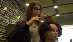 A cosmetology student works on a mannequin 