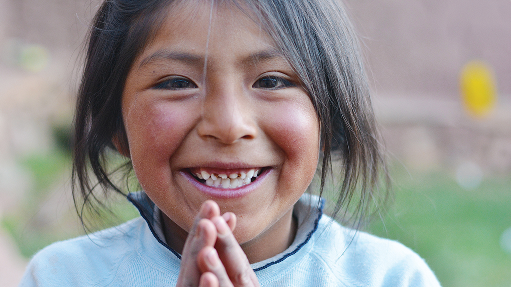 a native american girl with her hands clasped together smiles