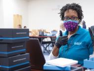 as school staff member in a mask holds up electronic equipment and gives a thumbs up to the camera