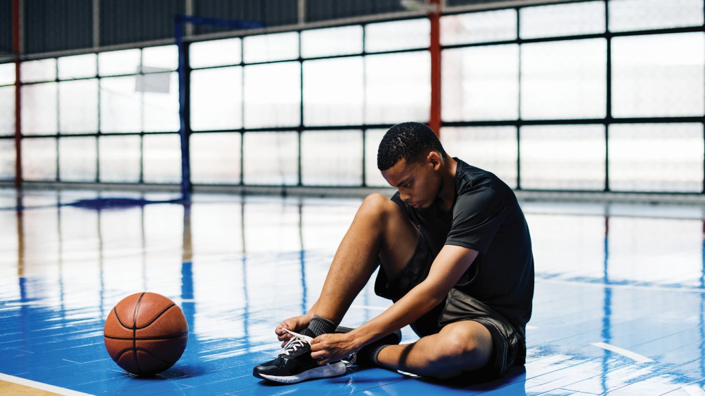 a student athlete ties his shoes in a gym, a basketball next to him