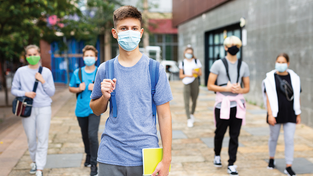 students walk outside on a school campus while wearing masks