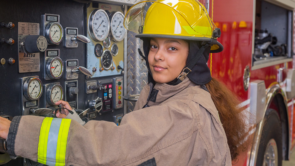 a student enrolled in a firefighter academy wears the firefighter uniform and works on a truck