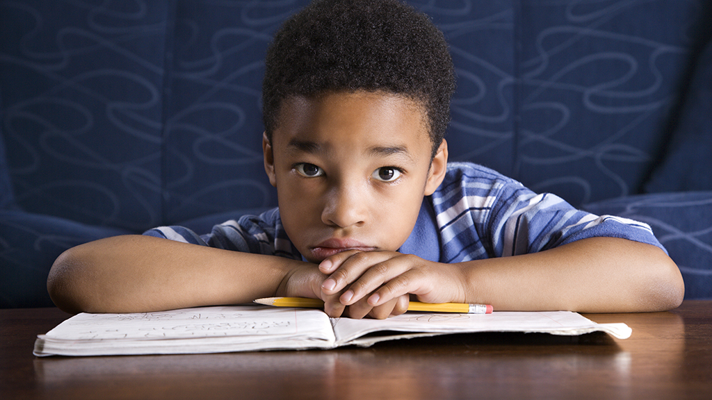 a boy, resting his head on his book, looks exhaustedly at the camera 