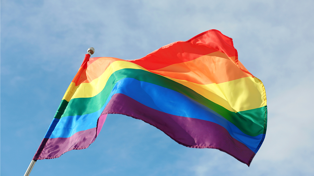 a rainbow pride flag flies against a blue sky