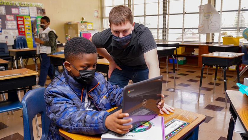 A student and teacher look at a laptop screen 