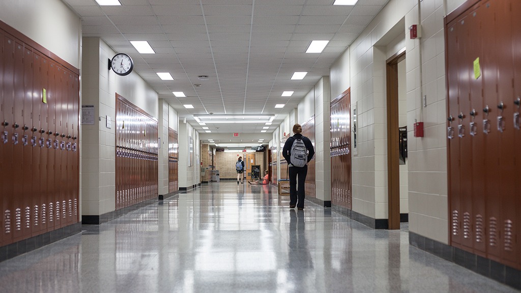 A few students walk along a  large high school hallway 