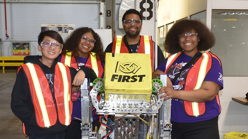 Four high school students wearing safety vests smile after winning a science competition.