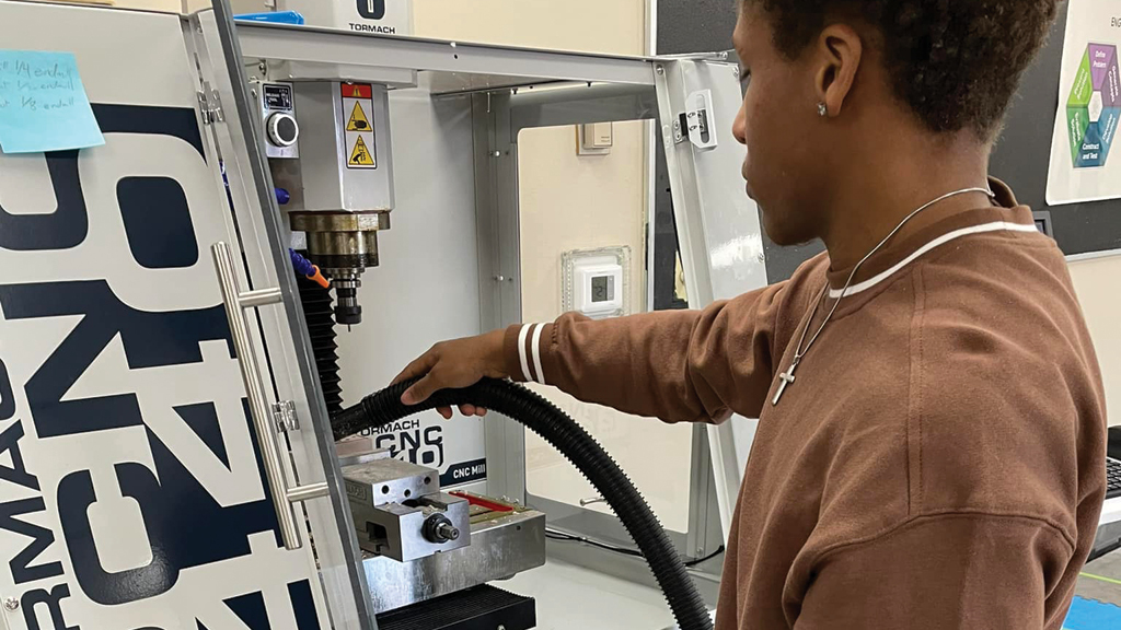 A high school student enrolled in a manufacturing class works at a computer numerical control mill.