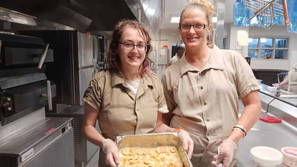 Two women enrolled in a jail education culinary program show the dessert that they made. 