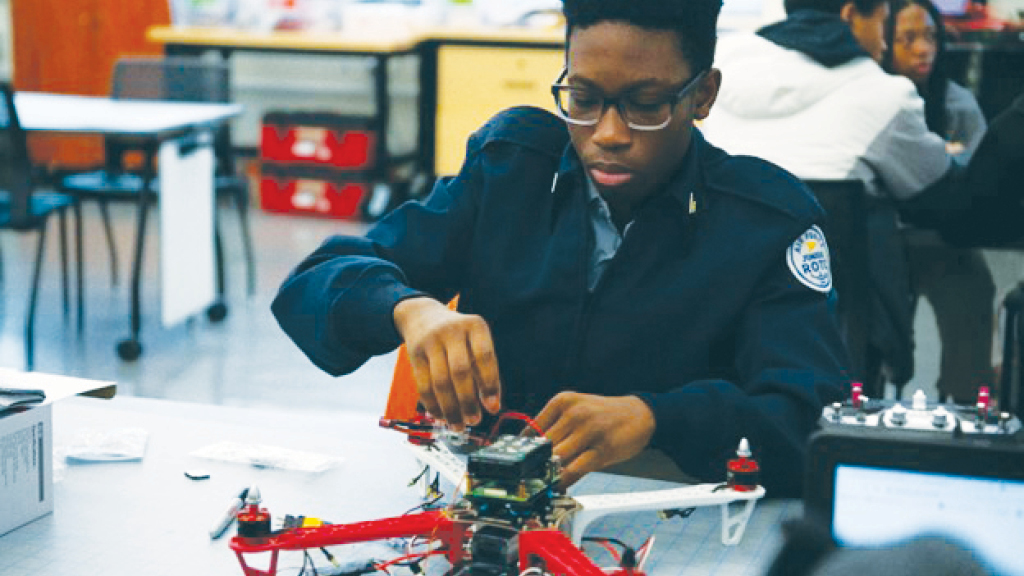 A high school student sits at a desk working on drone. 