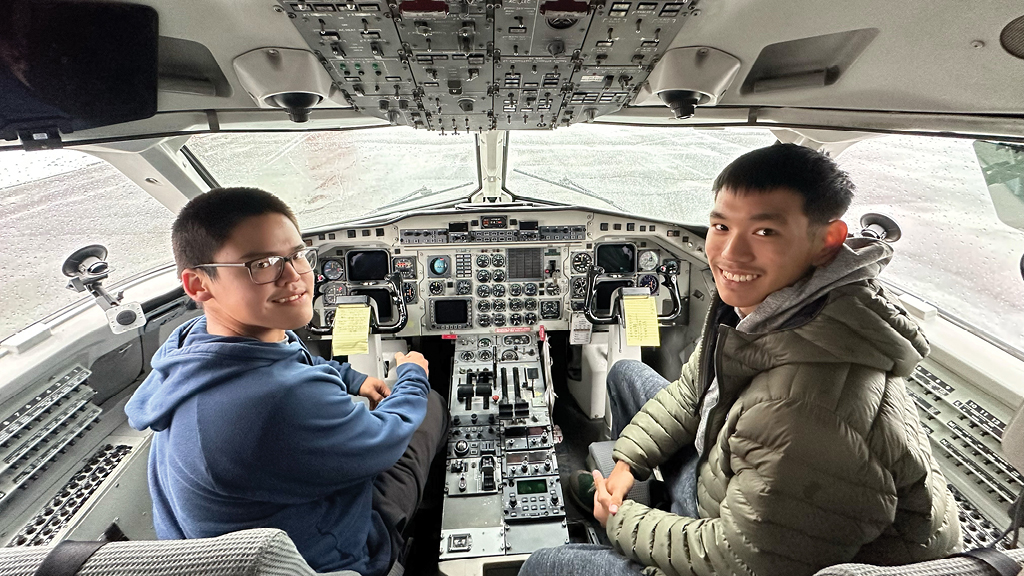 Two boys sit in the cockpit of an airplane. 