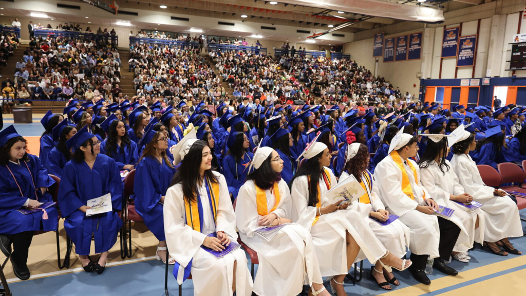 During a high school graduation ceremony, students sit in their seats dressed in their caps and gowns. 