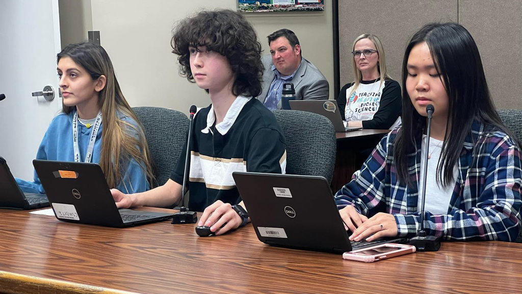 Three high school students sit at a table making a presentation to the school board. 