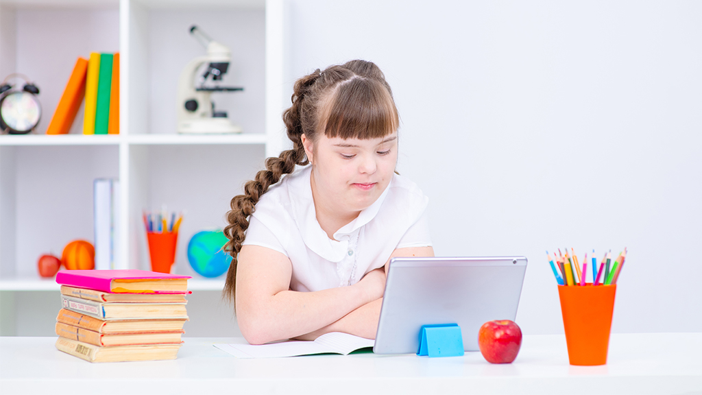a special education student sits at a home desk and uses a laptop for virtual learning