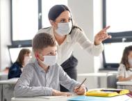 a teacher assists a student, both are wearing masks